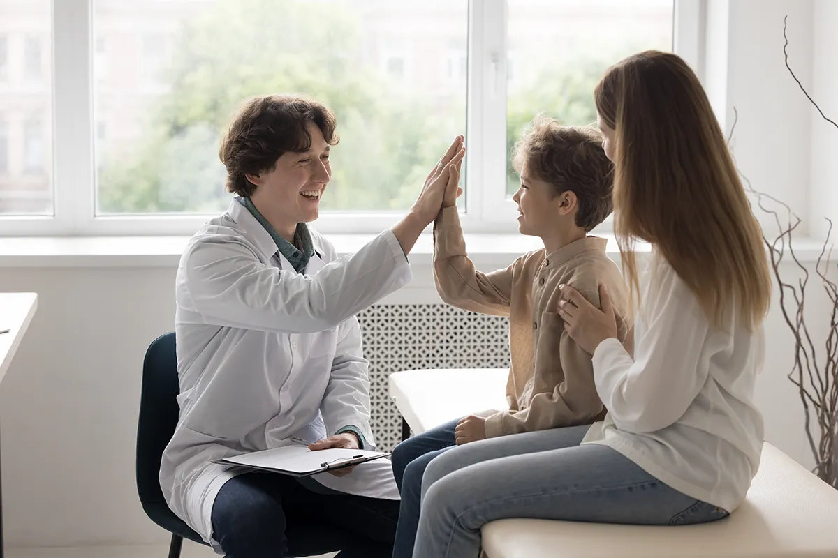 Pediatrician giving a child a high-five during an office visit with a parent nearby